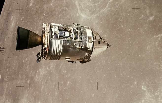 The command module centered orbiting over the lunar surface, cylindrical in shape with a pointed nose.