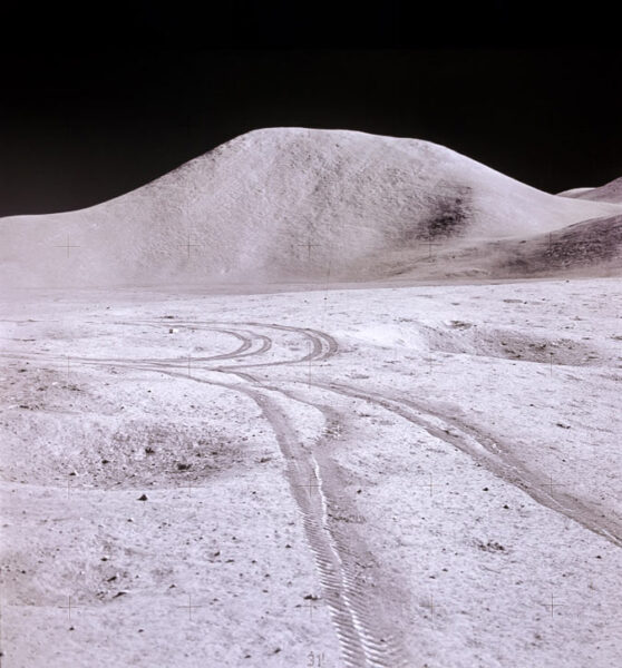 The lunar surface with rover trails and a hill in the background, which stands out drastically against the black background of space.