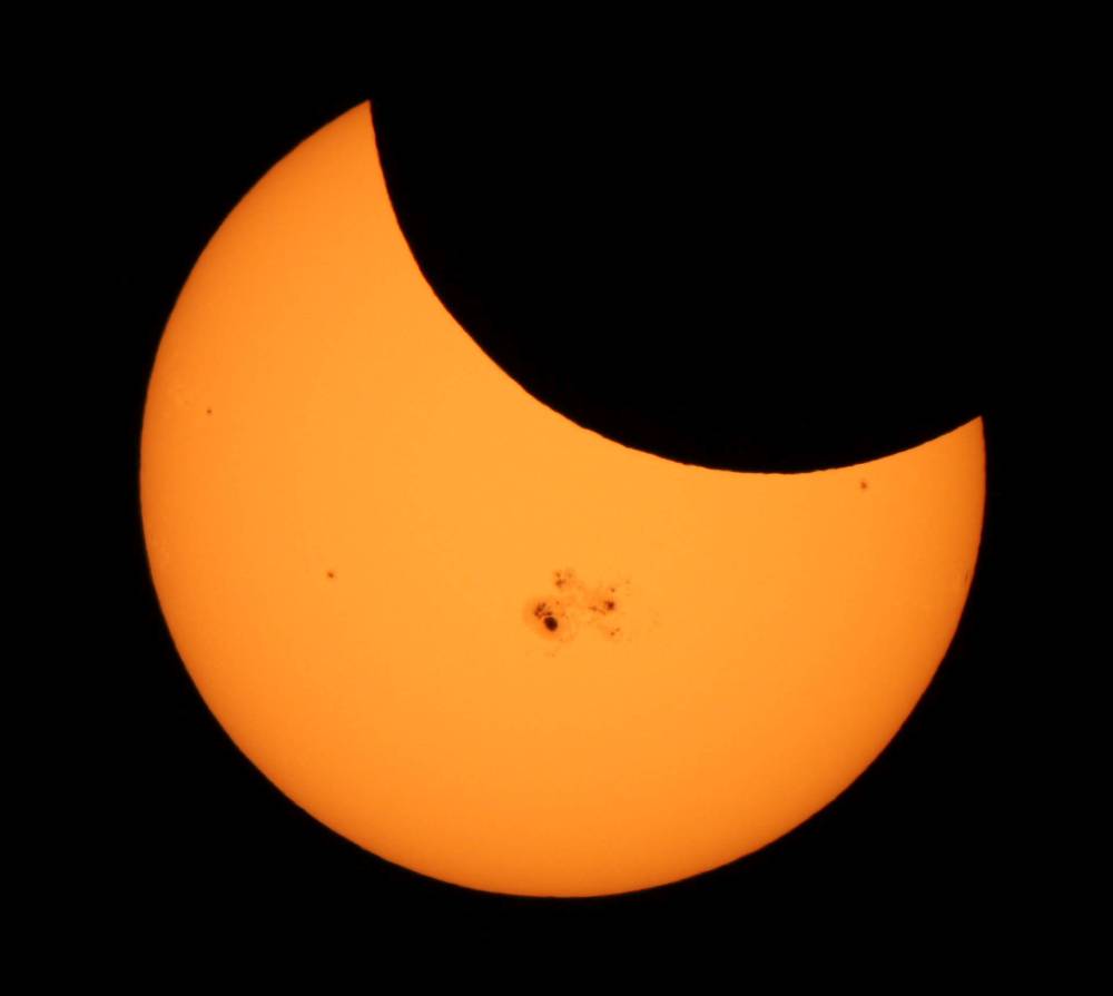 The Moon hovers in front of the left side of the Sun; the right side sports a complex of spots