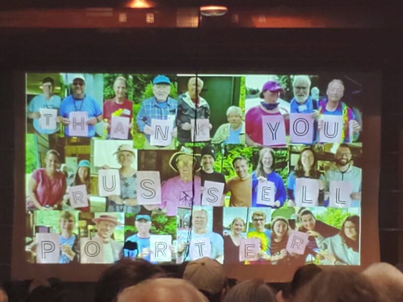 A slide from a slideshow depicting a collage of people holding up signs with letters on them that spell "Thank you Russell Porter"