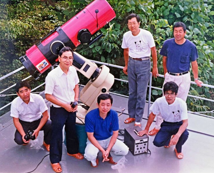 a group of people looking up from around a red telescope on a balcony