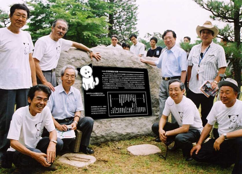  a group of people around a large stone with a black plague with writing in japanese on it