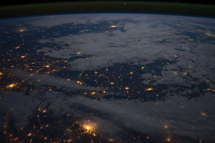 an aerial shot of the earth at night with bright yellow lights on a dark background