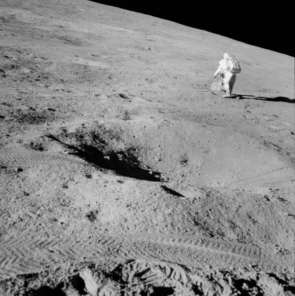 an astronaut walked the lunar surface in the distance, with a crater in the foreground