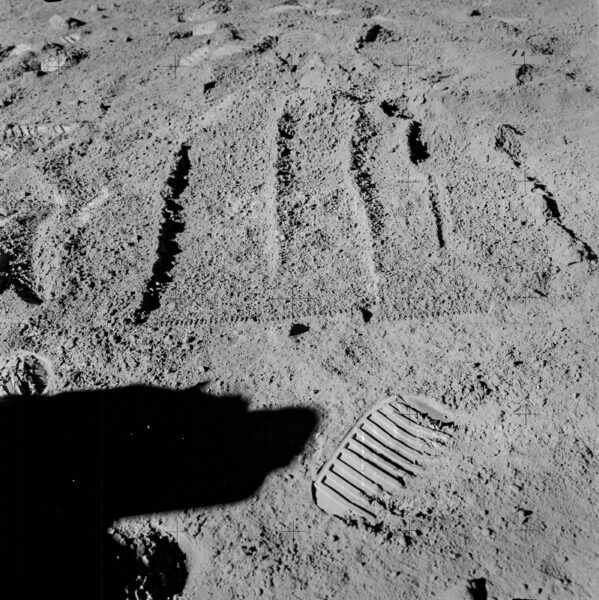 the imprints of a rake used to gather rocks from the lunar soil, next to an astronaut's footprint