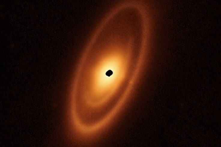 An orange oval extends from the 1 o’clock to 7 o’clock positions. It features a prominent outer ring, a darker gap, an intermediate ring, a narrower dark gap, and a bright inner disc. At the centre is a ragged black spot indicating a lack of data