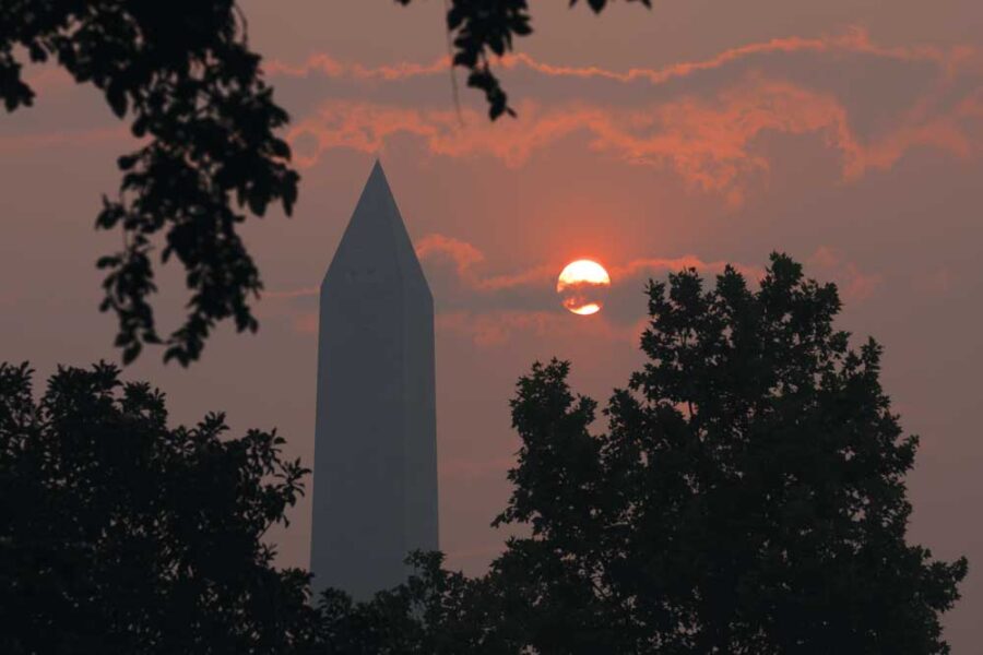 a sun setting behind a tall pointed building and trees