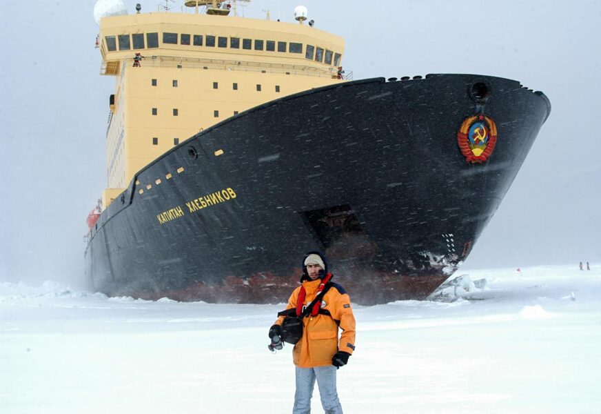 a man stands on ice in front of a cruise ship 