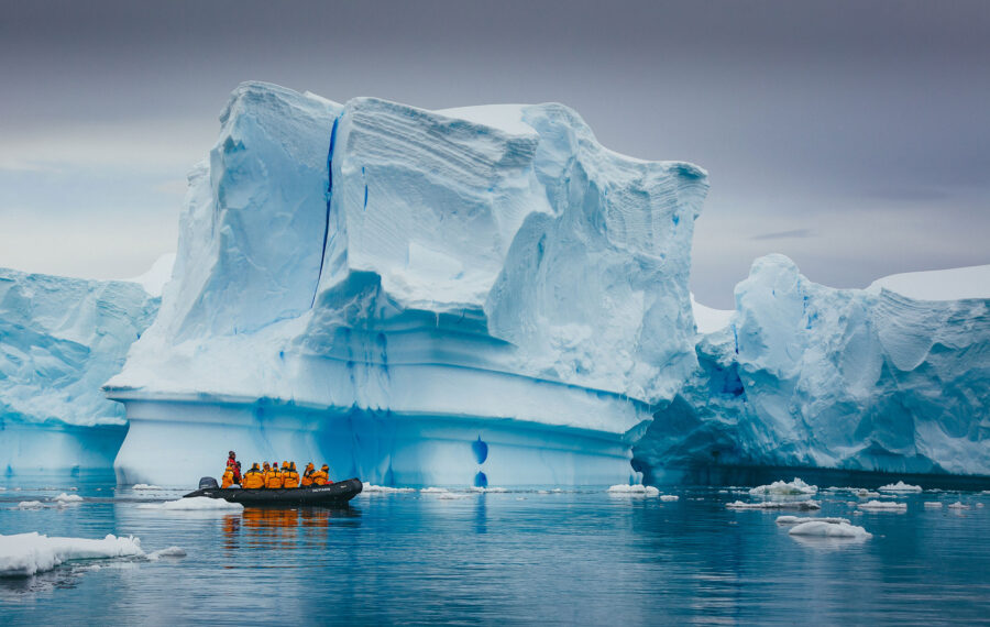 people in a small boat pass in front of a large iceberg