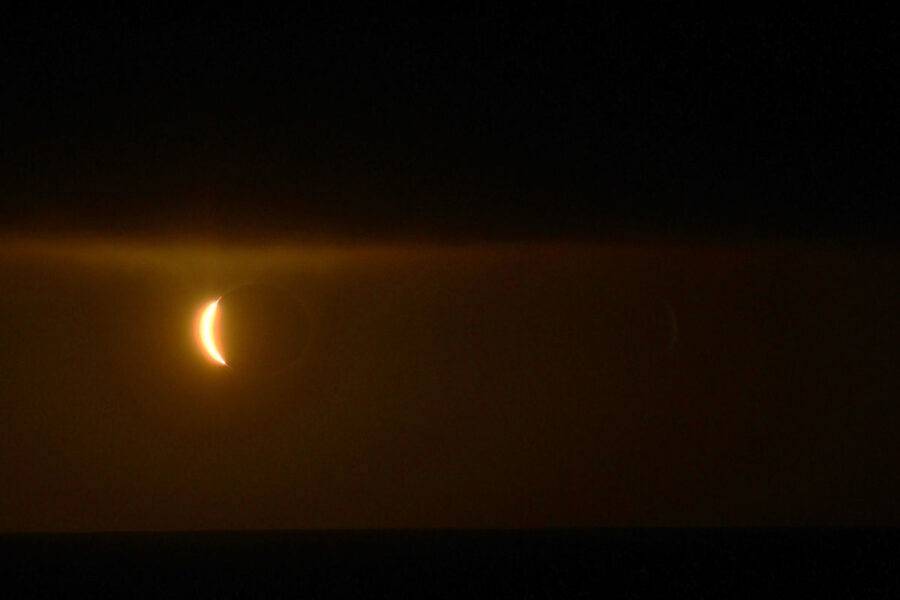 a sliver of orange light is visible on the left against a dark red and black background