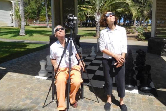 two people looking up at the sky with solar eclipse glasses on, one has a camera on a tripod