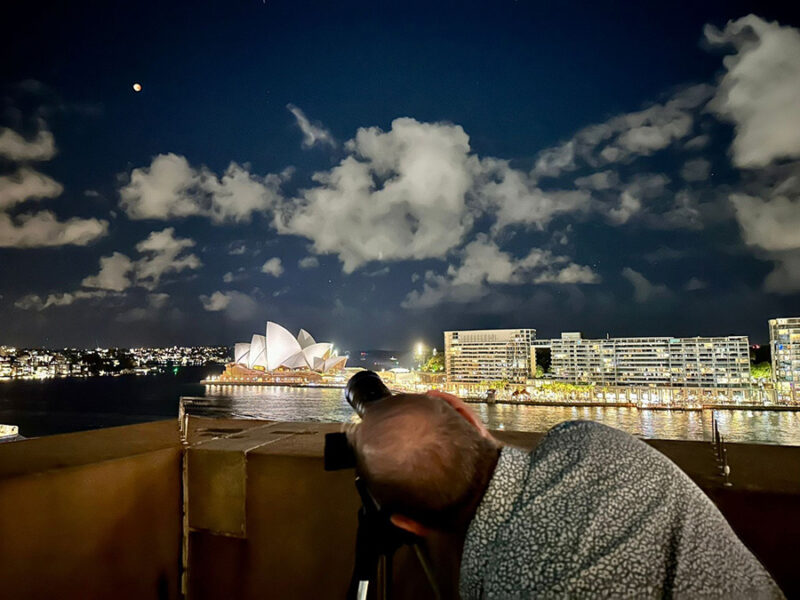 Man with his eye to the telescope overlooking the harbor in Sydney, Australia