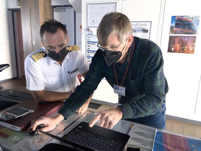 two men lean over a desk and work on a computer