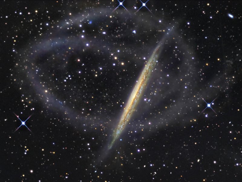 Photo of an edge-on galaxy encircled by a faint stream of stars.