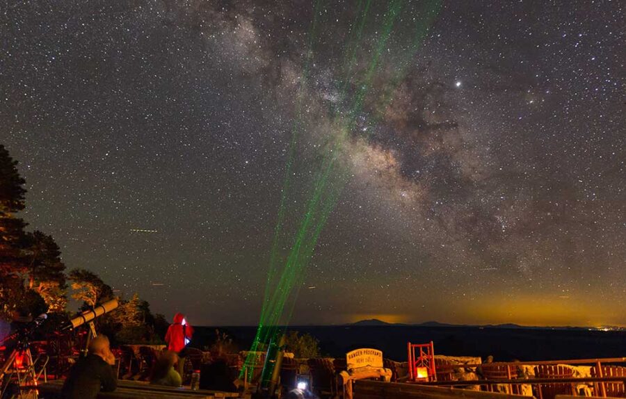 Green lasers shoot up in straight lines over nighttime crowd, Grand Canyon in background