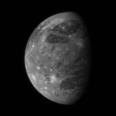 Ganymede shown in grey with white spots on it against a black background
