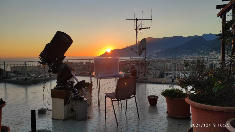 a telescope on a deck oberlooking water with the sun setting behind a mountain