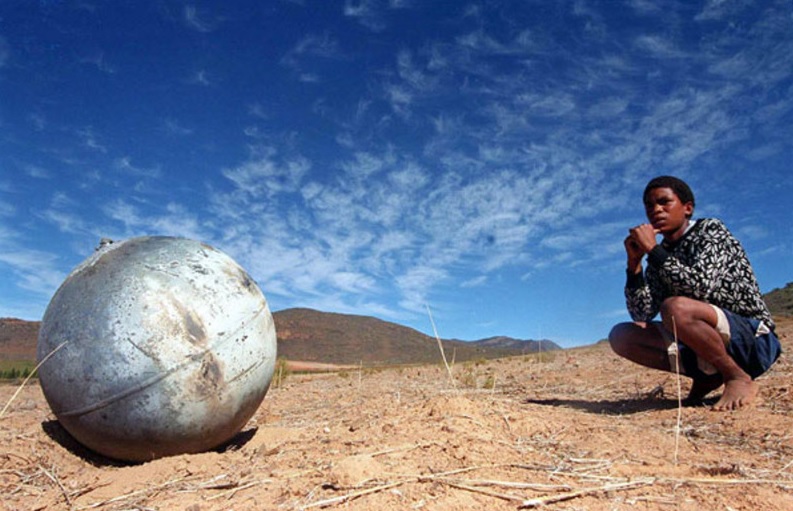 Boy sits next to globular space debris that landed on the ground
