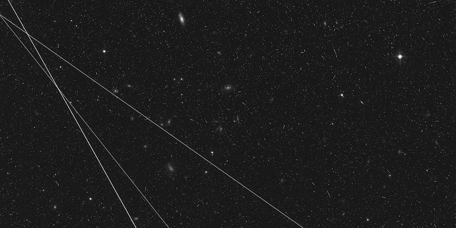 Three diagonal trails at different angles pass through image dotted with small galaxies