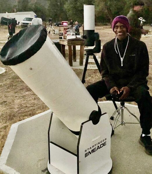 a man sitting at a large telescope in a field