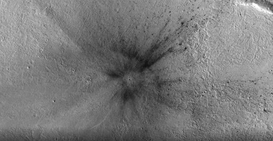 Grayscale image shows small dark dot surrounded by rays of dark gray ejecta