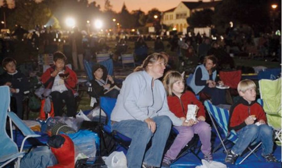 an adult and two children look at something offscreen while sitting in front of a crowd of people