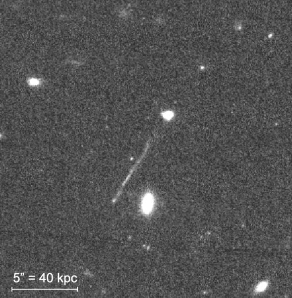 Black-and-white image shows stream of light emanating from blob of light that represents the galaxy