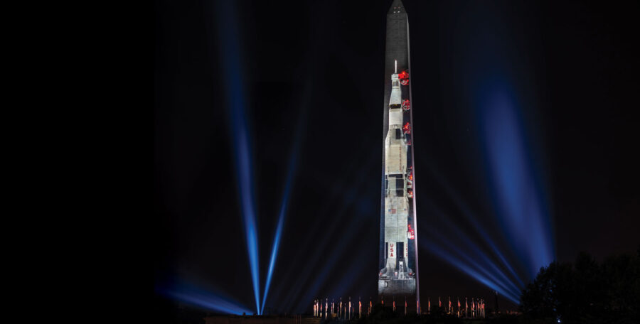 a tall thin building at night with the image of a rocket projected onto it