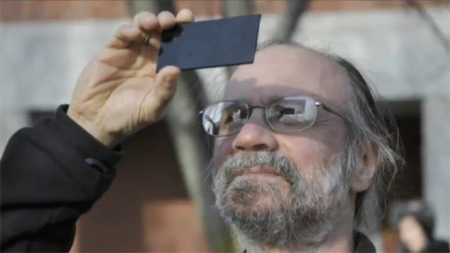 a man holds a piece of dark glass up to the sun